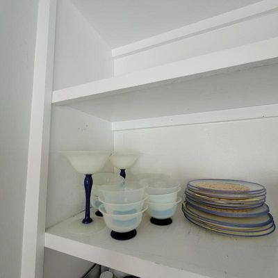 Vintage frosted glass dessert cups with cobalt blue stems and bases, displayed alongside a stack of matching glass plates on a white shelf.