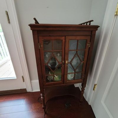 Vintage mahogany curio cabinet featuring glass-front doors with diamond-patterned wood mullions, turned legs, and a lower display shelf.
