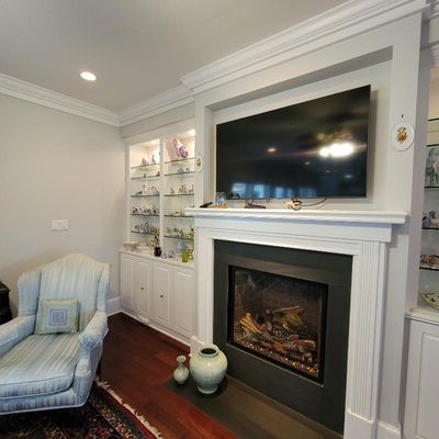 Modern gas fireplace with a white mantel, a wall-mounted flat-screen television, and a built-in display cabinet filled with porcelain...