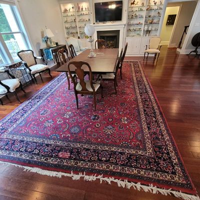 Large Persian-style area rug with a red field, intricate floral motifs, and a dark blue border, shown under a wooden dining set.