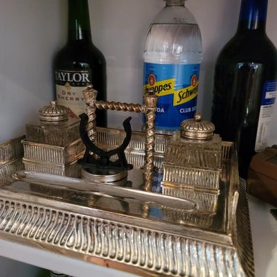 Vintage silver-plated double inkwell stand with two glass inkwells, featuring a decorative central handle and a pen rest tray.