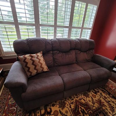 Plush three-seat reclining sofa in dark brown microfiber upholstery, featuring a tufted back and a chevron-patterned accent pillow.