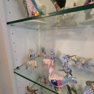 Collection of Herend porcelain figurines featuring their signature fishnet pattern, displayed on glass shelves.