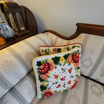 Pair of vintage needlepoint throw pillows with floral designs, resting on a classical-style upholstered sofa.