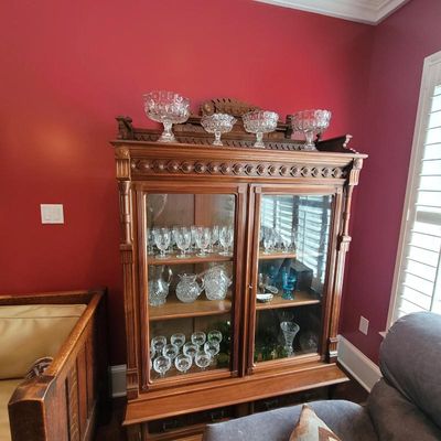 Antique carved oak china cabinet with glass doors, displaying a collection of crystal stemware, pitchers, and serving bowls.