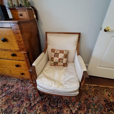 Vintage wood-framed armchair with off-white damask upholstery and carved details, paired with a small patchwork throw pillow.