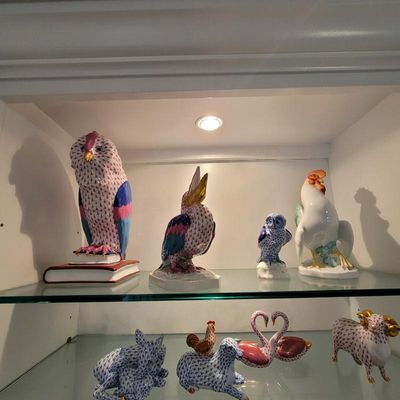Collection of Herend porcelain figurines, including owls, a toucan, a rooster, and other animals, displayed on glass shelves.