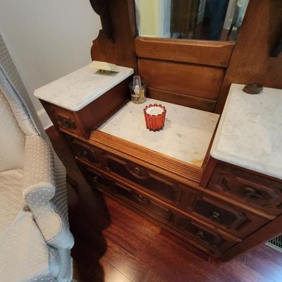 Antique Eastlake-style wooden dresser featuring a three-piece white marble top, integrated mirror frame, and carved drawer pulls.
