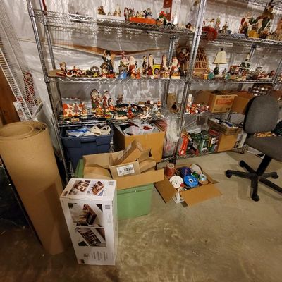 Assorted Christmas decorations, including Santa figurines and holiday village pieces, displayed on metal wire shelving alongside storage...