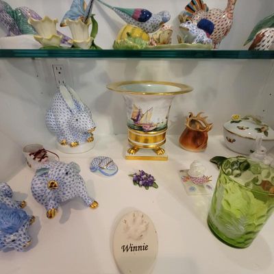 Collection of Herend porcelain figurines, including a blue fishnet rabbit and pig, alongside a footed vase with gold trim and sailboat...