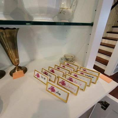 Set of vintage porcelain place card holders with gold-gilded borders and floral details, displayed alongside a brass vase and white...