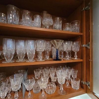 Large collection of cut crystal glassware, including goblets, tumblers, and a single blue-stemmed martini glass, displayed on wooden...