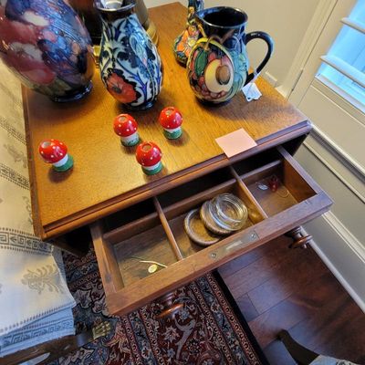 Vintage wooden side table with an open drawer containing small glass jars, topped with colorful art pottery vases and small mushroom...