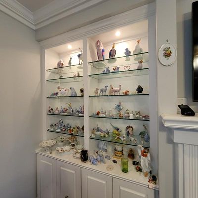 A large collection of porcelain figurines, including Herend and other fine makers, displayed on glass shelves in a built-in white cabinet.