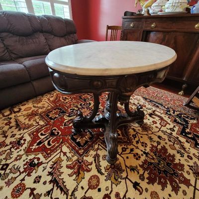 Victorian-style oval parlor table featuring a white marble top and an ornately carved dark wood pedestal base.