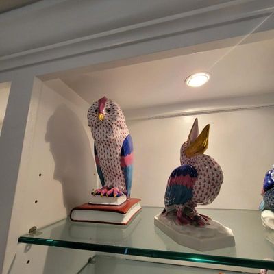 Two Herend porcelain bird figurines, including an owl perched on books and a pelican, featuring the signature hand-painted fishnet...