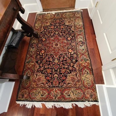Traditional Persian-style area rug featuring an intricate floral medallion design in red, navy, and gold tones with fringed edges.