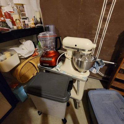 KitchenAid stand mixer in cream finish with stainless steel bowl, alongside a red KitchenAid food processor, displayed on a vintage...