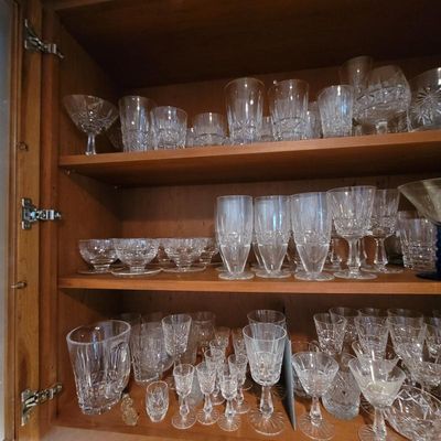 Large collection of vintage cut crystal glassware, including goblets, tumblers, sherbet dishes, and a pitcher, neatly arranged on wooden...