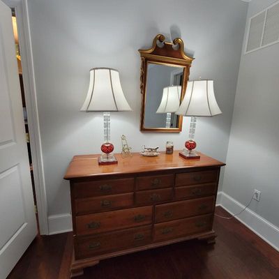Traditional wooden dresser with brass hardware, paired with a matching set of crystal and red glass table lamps and a gold-framed wall...