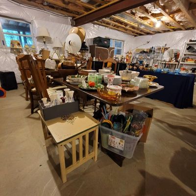 Assorted vintage kitchenware, glassware, and dining furniture displayed in a basement estate sale setting.