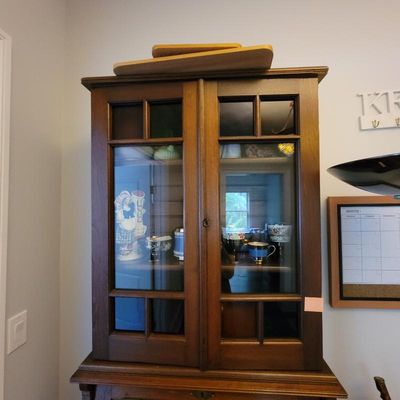 Vintage wooden hutch top with glass-front double doors, displaying various ceramic and glassware items inside.