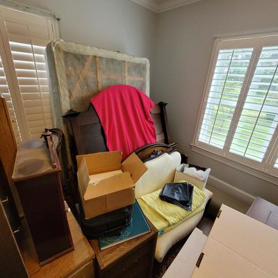 Assorted bedroom furniture including a dark wood headboard, a mattress, and a small upholstered settee, shown with various packing boxes...