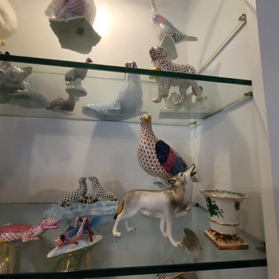 Collection of Herend porcelain figurines, including a howling wolf, birds, and seals, displayed on glass shelves.