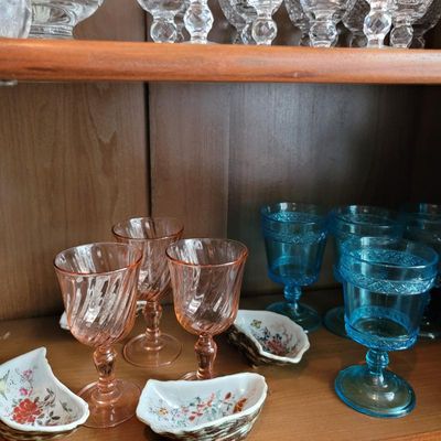 Assorted vintage glassware including pink swirl-patterned goblets, blue pressed-glass goblets, and small floral-patterned ceramic dishes...