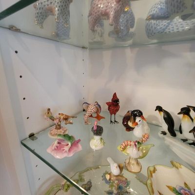 Collection of miniature porcelain animal figurines, including birds, a frog, and penguins, displayed on glass shelves.