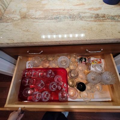 Assorted glassware collection, including cut glass bowls, tumblers, and small dishes, organized inside a wooden kitchen drawer.