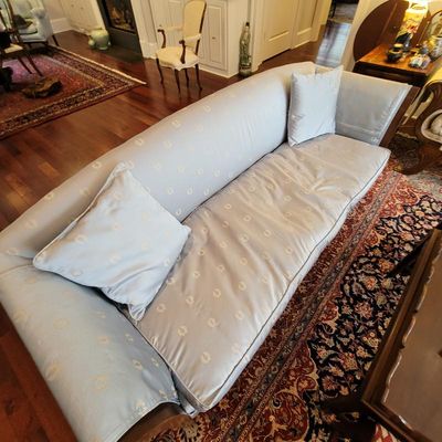 Traditional camelback sofa upholstered in a light blue patterned damask fabric, featuring two matching throw pillows and a single seat...