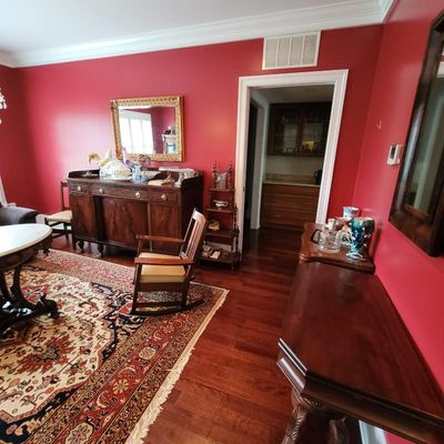 Traditional dining room featuring a large mahogany sideboard, a wooden rocking chair, a patterned area rug, and a gold-framed wall mirror...