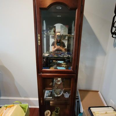 Traditional cherry wood curio cabinet featuring glass shelves, a mirrored back, and interior lighting, filled with various collectibles.