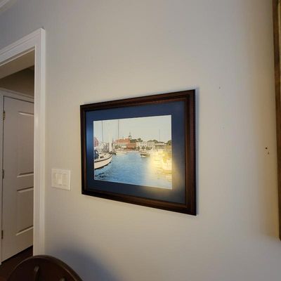 Framed and matted print depicting a harbor scene with boats, housed in a dark wooden frame with a blue mat.