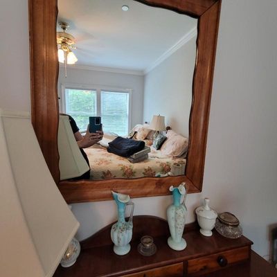 Large rectangular wall mirror with a wavy, natural-edge wood frame, shown hanging above a dresser with decorative glassware.