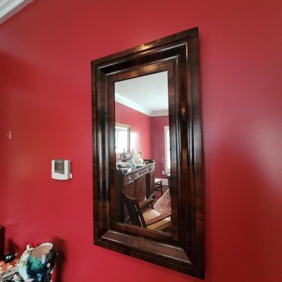 Large rectangular wall mirror featuring a wide, dark wood frame with a polished finish, mounted on a red wall.
