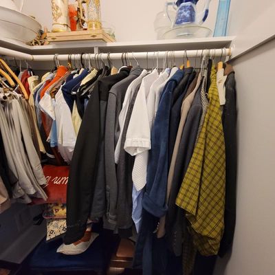 Assorted men's clothing including jackets, button-down shirts, and a yellow plaid shirt hanging in a closet, with decorative...