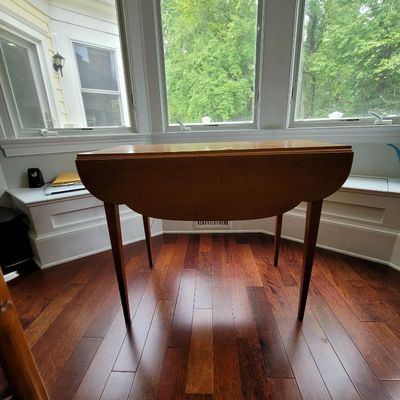 Mid-century modern wooden drop-leaf table with tapered legs, shown in its folded position on a hardwood floor.