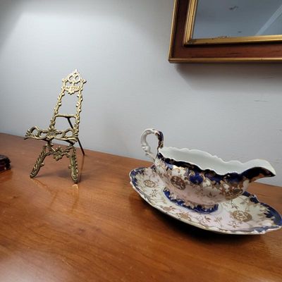Antique porcelain gravy boat with matching underplate featuring cobalt blue and gold gilt accents, displayed alongside an ornate brass...