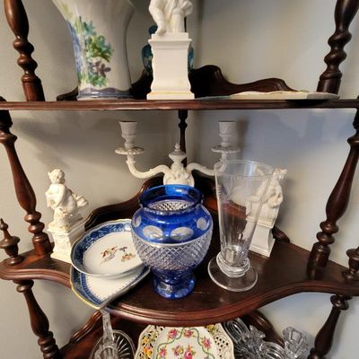 Assorted vintage glassware and porcelain collectibles, including a cobalt blue cut-to-clear glass vase, displayed on a dark wood corner...