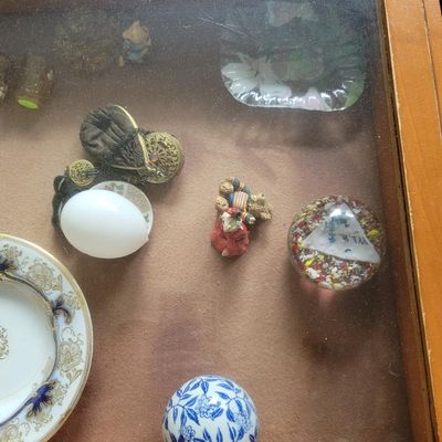 Assorted vintage collectibles displayed in a glass-top case, including a millefiori paperweight, a small porcelain dish with gold trim, a...