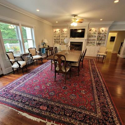 Large traditional Persian-style area rug with intricate floral motifs in red, blue, and cream, anchoring a formal dining room set with a...