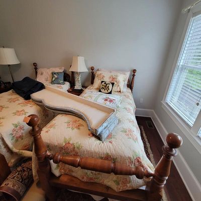 Pair of vintage wooden twin beds with turned posts, dressed in floral quilts and accompanied by matching table lamps.