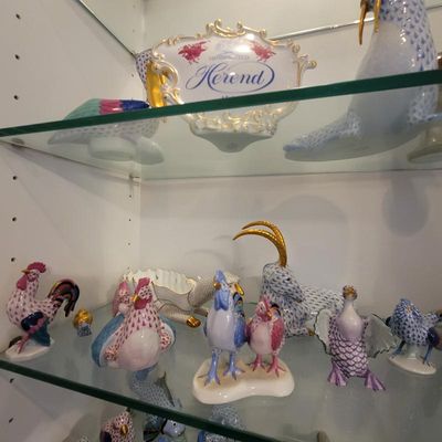 Collection of Herend hand-painted porcelain animal figurines, featuring their signature fishnet pattern, displayed on glass shelves.