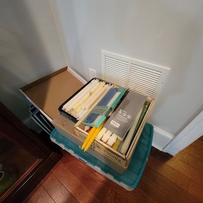 Assortment of taper candles in various colors and sizes, packaged in boxes and stored on a plastic bin.