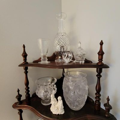 Assorted vintage glassware, including a cut-glass decanter, lidded sugar bowl, and frosted glass vase, displayed on a two-tiered wooden...