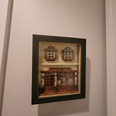 Three-dimensional shadow box wall art depicting a European-style saloon bar storefront, housed in a dark wooden frame.