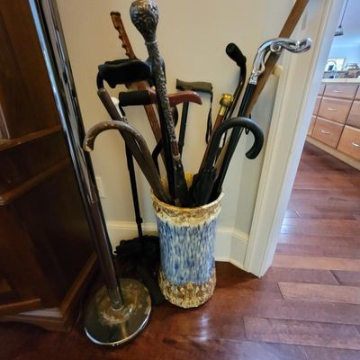Collection of vintage and modern walking canes, umbrellas, and crutches displayed in a blue and white glazed ceramic umbrella stand with...