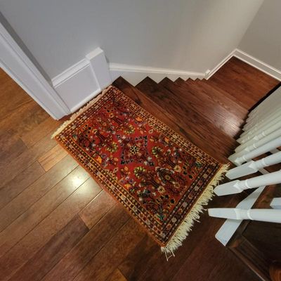 Small Persian-style accent rug featuring a vibrant red field with intricate floral and tree motifs, finished with a fringed border.
